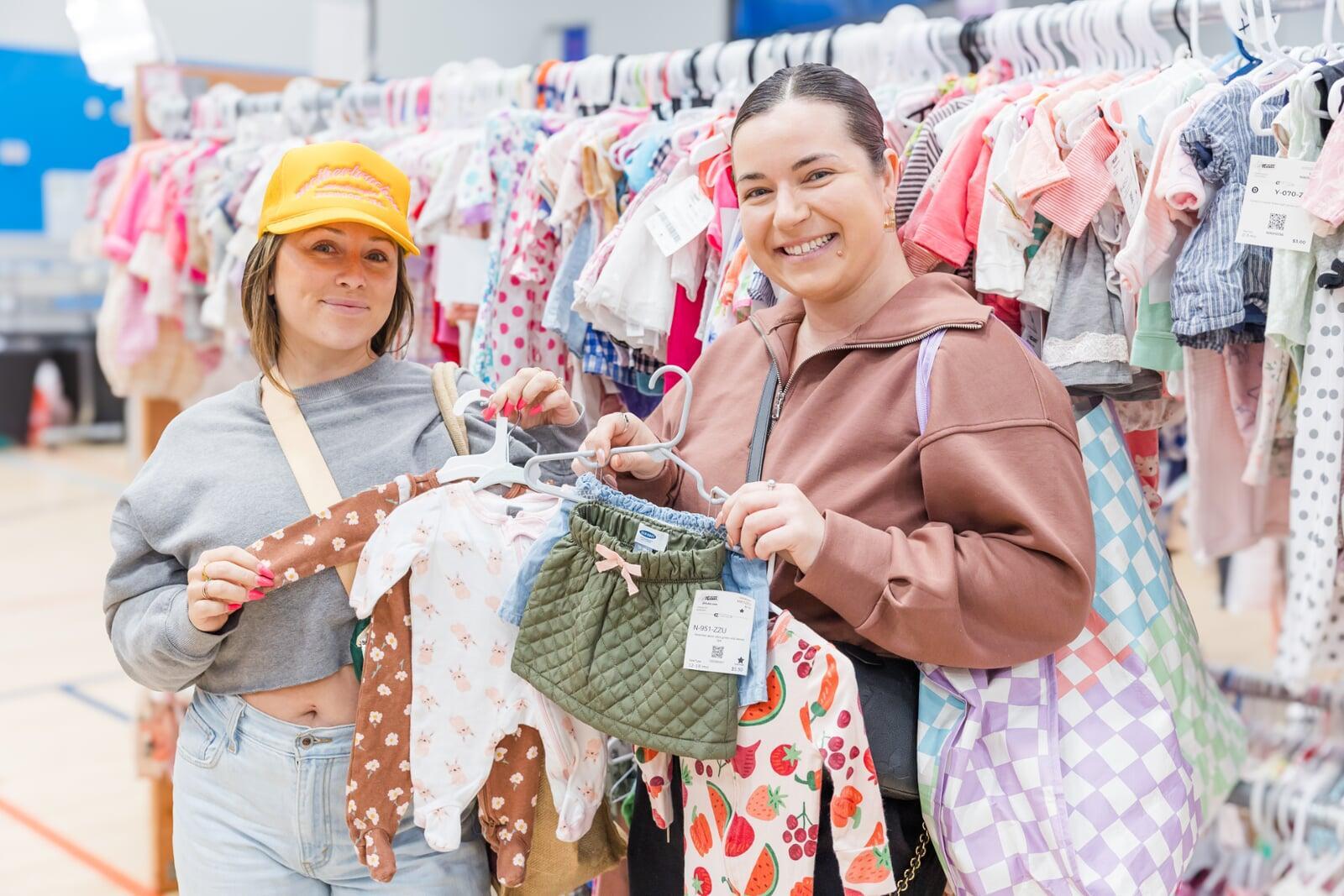 Two friends shop together—one mom wears her baby girl—as they find great deals at their local JBF sale.
